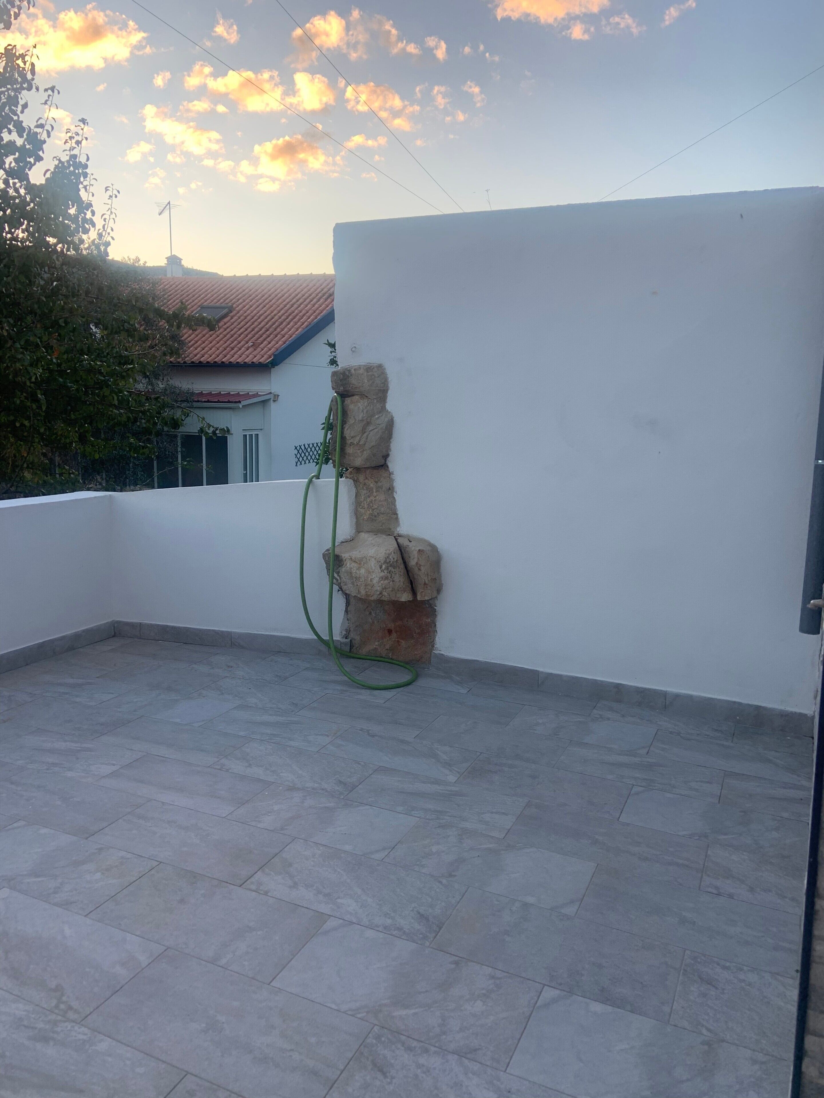 Une terrasse sur le toit, dotée d’une structure en pierre, d’un tuyau d’arrosage vert et d’un sol carrelé.