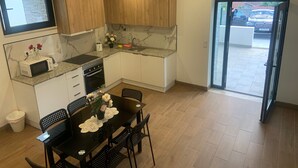 A modern kitchen with wooden cabinets, a granite countertop, a dining table with chairs, and a view of the outside through a glass door.