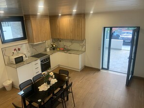 A modern kitchen with wooden cabinets, a granite countertop, a dining table with chairs, and a view of the outside through a glass door.