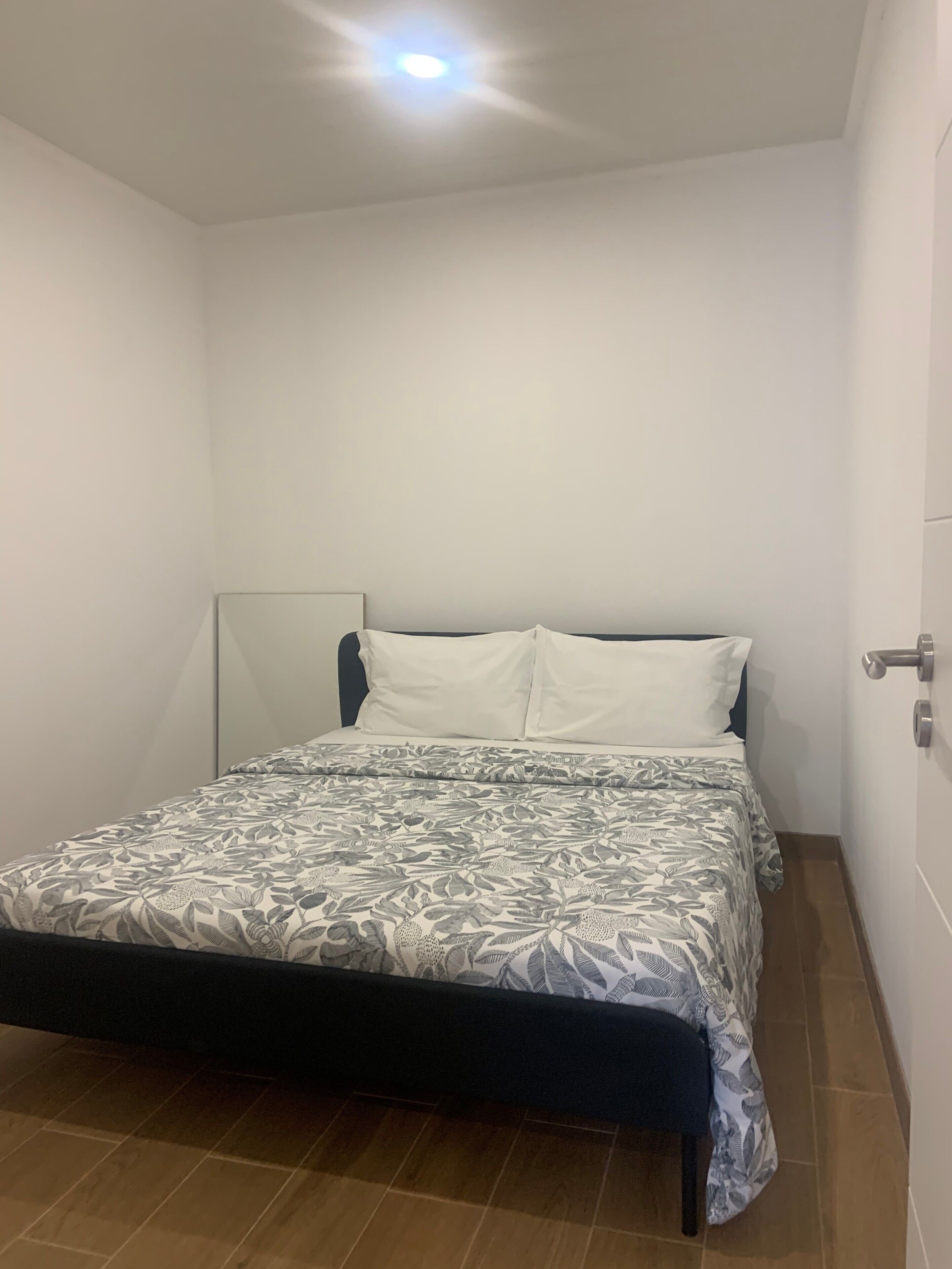A single bed with a patterned bedspread, a bedside table, and a door on the right.