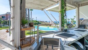Cucina esterna con lavello, ripiano in legno e vista su piscina e oceano.