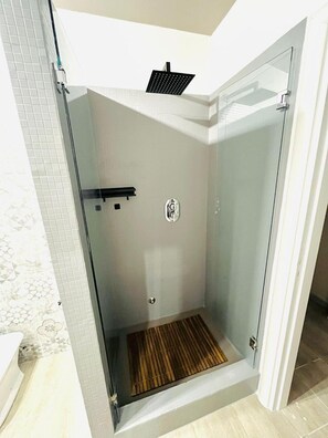 Een glazen douchecabine met een houten vloer, een handdoekrek en een bedieningspaneel aan de wand.