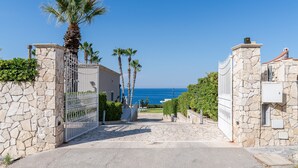 Un cancello con mura in pietra, palme e vista sul mare.