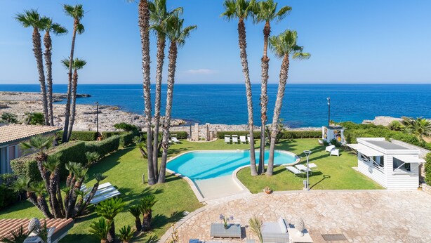 Area piscina con palme, cielo azzurro e vista sul mare.