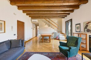 Ein geräumiger Wohnbereich mit Holzboden, einer Couch, einem Sessel, einem Esstisch und einer Treppe, die zu einer oberen Etage führt.
