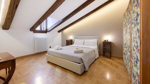 Slaapkamer met een houten plafond, een bed met wit beddengoed, een radiator, een kleine tafel en een wand met bloemenbehang.