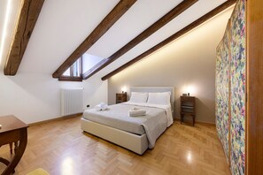 Slaapkamer met een houten plafond, een bed met wit beddengoed, een radiator, een kleine tafel en een wand met bloemenbehang.