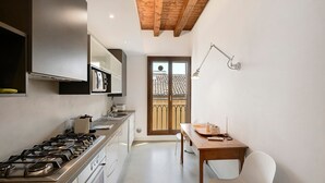 Een keuken met een gasfornuis, kastjes en een eethoek met een tafel en stoelen.