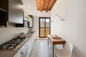 Een keuken met een gasfornuis, kastjes en een eethoek met een tafel en stoelen.