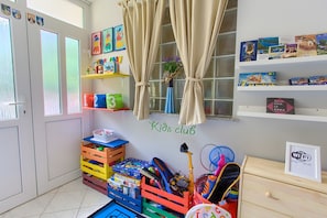 Habitación infantil con un cartel de 'Kids club', cajas de almacenamiento, estanterías llenas de juguetes y un cartel de 'Free WiFi'.