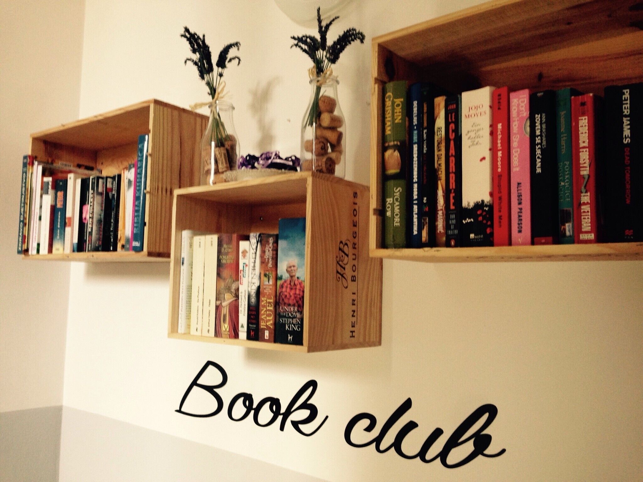 Un mur orné de trois étagères en bois, chacune portant l’inscription « Club de lecture » et contenant des livres ainsi que de petits objets décoratifs.