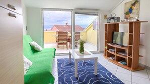 A living room with a green sofa, a white coffee table, a wooden TV stand, and a view of a balcony with a table and chairs. - Apartment 'Daniela with Sea View' with Sea View, Wi-Fi and Air Conditioning (Porat)