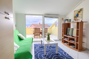 Una sala de estar con un sofá verde, una mesa de centro blanca, un mueble de televisión de madera y vistas a un balcón con mesa y sillas.
