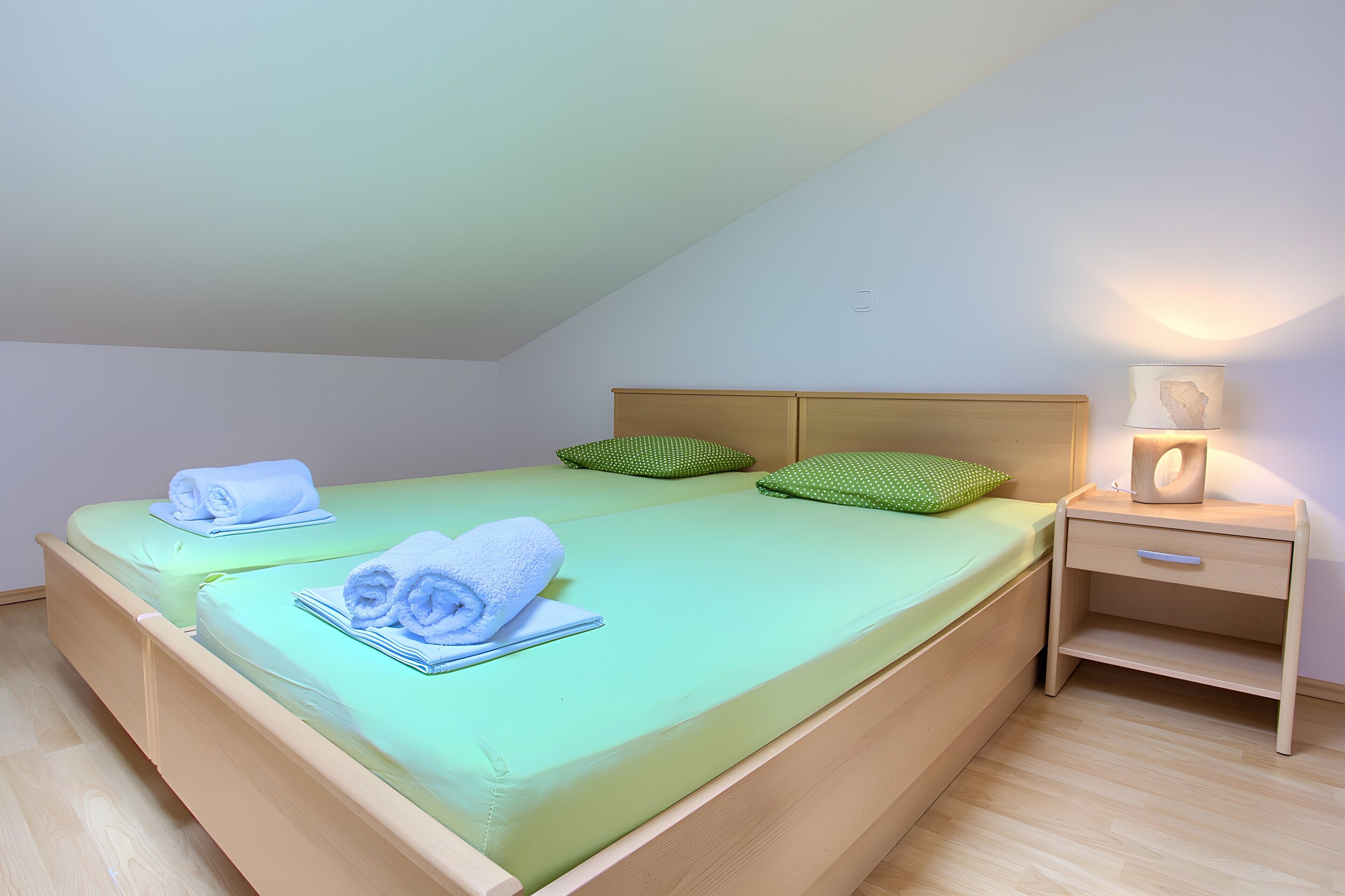 Ein Einzelbett mit grüner Bettwäsche, einem Holz-Kopfteil und einem Nachttisch mit Lampe.