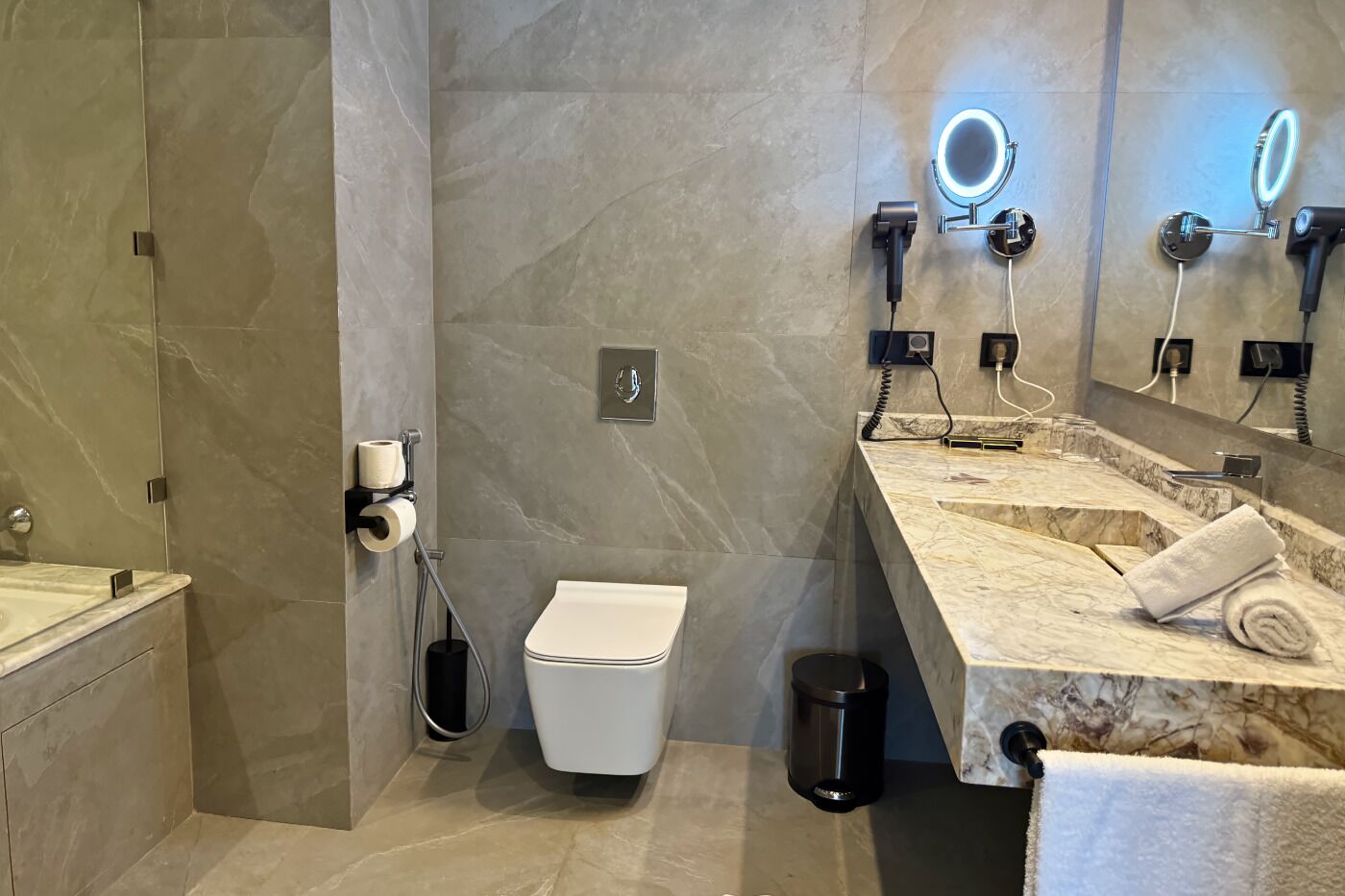 Une salle de bain moderne avec un meuble-lavabo en marbre, des toilettes, un sèche-mains et un porte-serviettes.