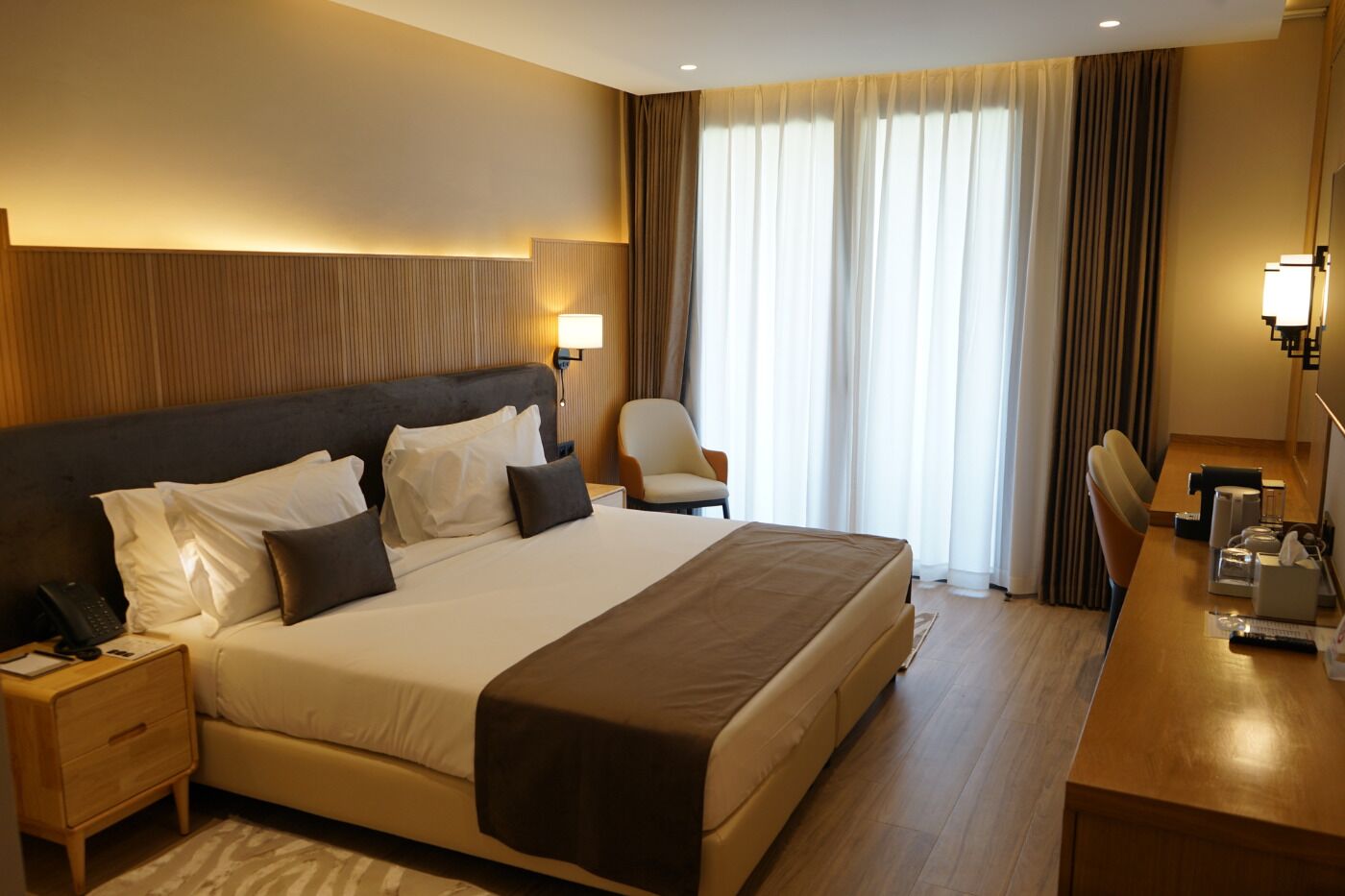 A hotel room with a large bed, bedside tables, a desk, and a chair.