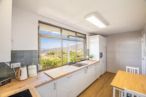 Une cuisine dotée d’une grande fenêtre, de meubles blancs, d’un plan de travail en bois et offrant une vue sur un paysage montagneux.