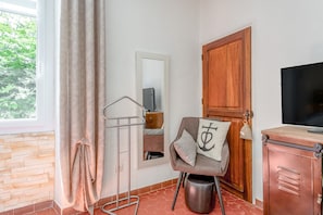 Een kamer met een houten deur, een spiegel, een stoel met kussen, een televisie en een raam met gordijnen.