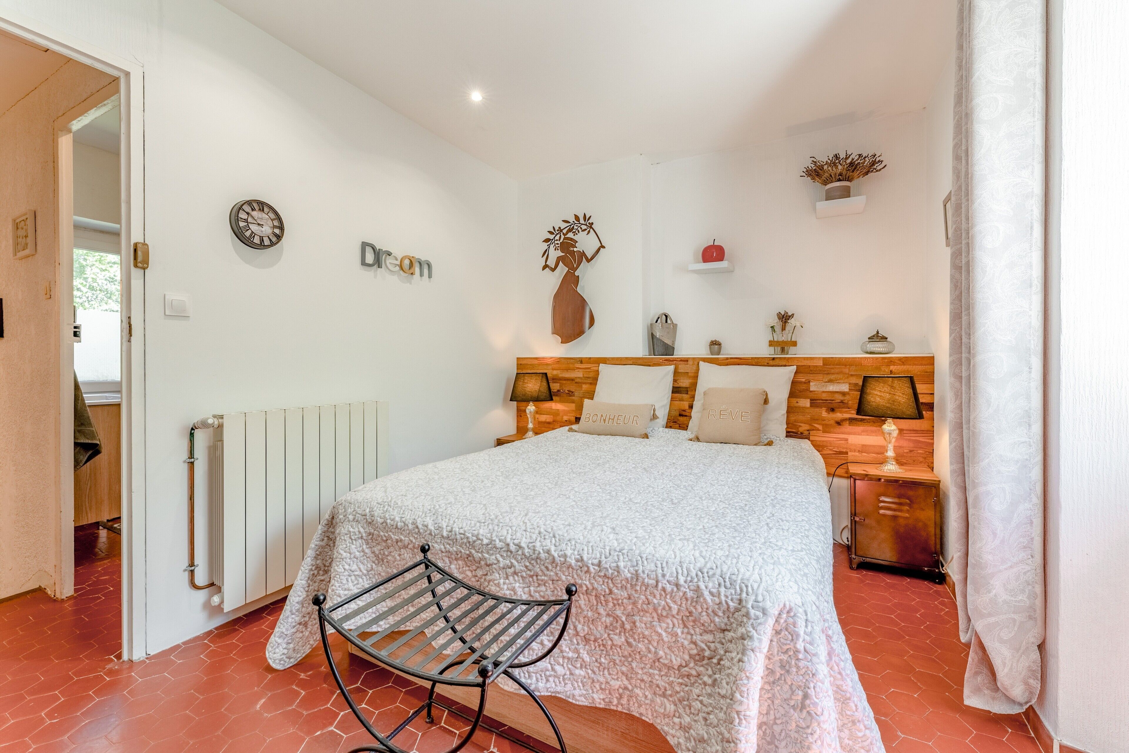 Ein Schlafzimmer mit einem Bett, einem hölzernen Kopfteil, einem Nachttisch mit Lampe, einem Heizkörper und einer Wanduhr.
