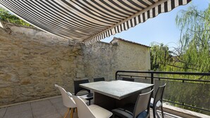Eine Außenpatio mit Tisch und Stühlen, einem Streifenmarkisenvorzelt, Steinmauern und Blick auf Grünflächen.