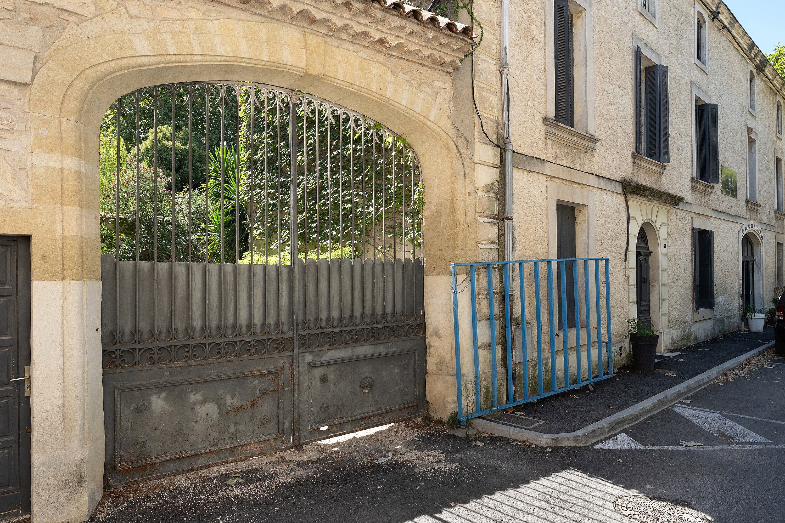 Un arc en pierre surmonté d’un portail en métal, une clôture en métal bleue et un bâtiment doté de nombreuses fenêtres et d’une porte.