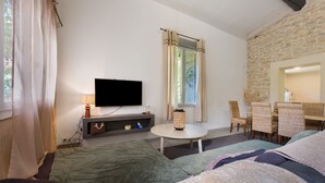 Ein gemütliches Zimmer mit Fernseher, einem kleinen Tisch, Korbstühlen und einer Steinwand.