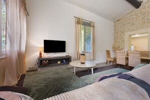 A cozy room with a flat-screen TV, a small table, wicker chairs, and a stone wall.