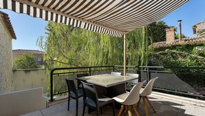 Eine Terrassengruppe mit Tisch und Stühlen, umgeben von einem Metallgeländer, unter einem gestreiften Markisenvorzelt.