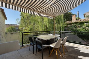 An outdoor patio with a table and chairs, surrounded by a metal railing, under a striped awning.