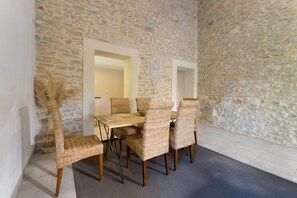A dining area with a stone wall, a wooden table, and wicker chairs. - Authentic Cottage with Terrace and Private Garden in Languedoc (Bernis)