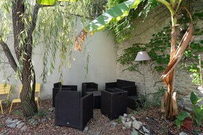 An outdoor seating area with wicker furniture, a lamp, and a stone wall. - Authentic Cottage with Terrace and Private Garden in Languedoc (Bernis)