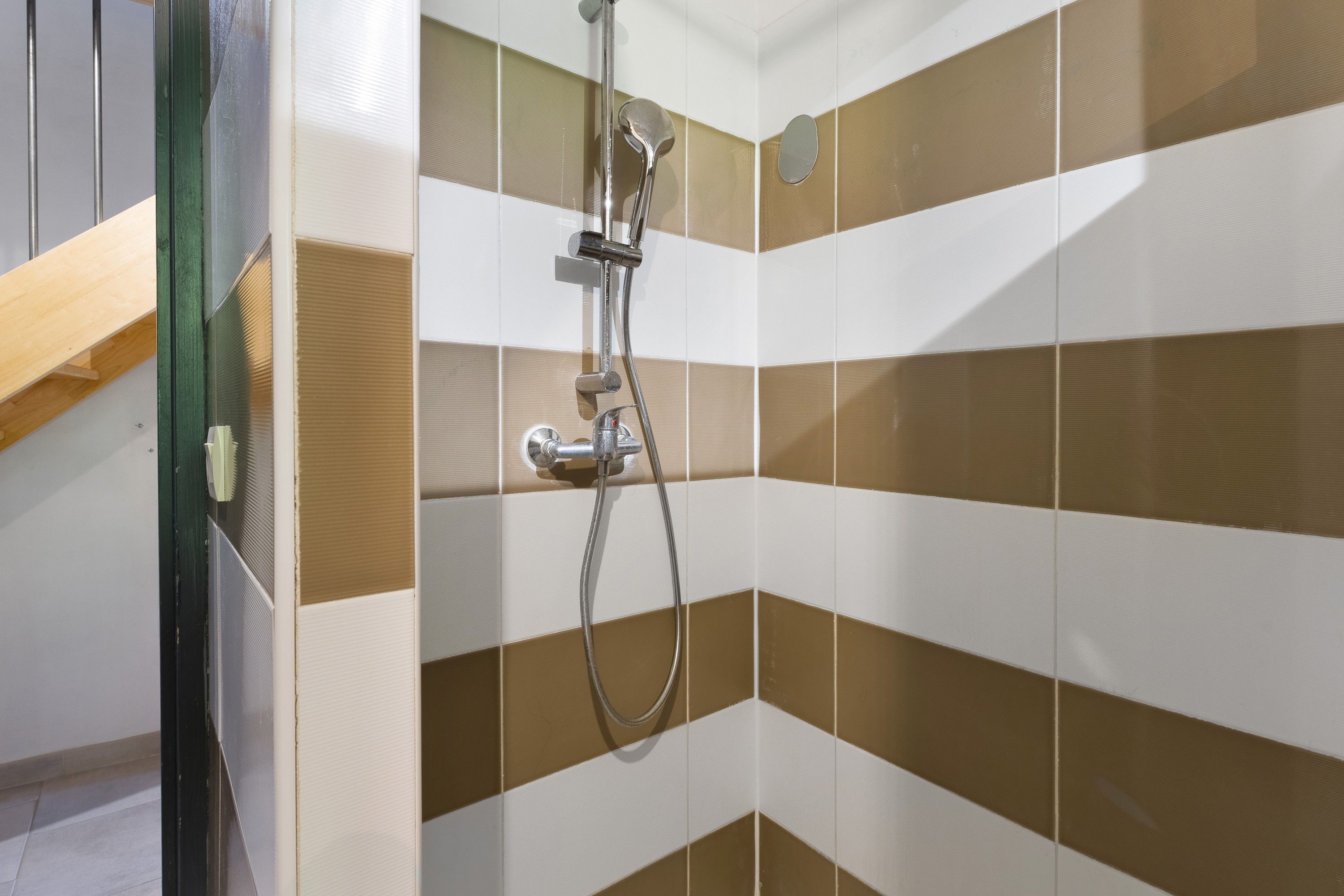 Une douche équipée d’un pommeau de douche à main et d’un robinet fixé au mur.