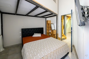 A bedroom with a bed, a bedside table, a wall-mounted TV, and a wooden shelving unit.