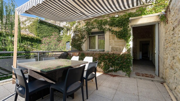 Eine Terrasse im Freien mit Tisch und Stühlen, einem Streifen-Jalousie und einer Steinmauer mit Grünpflanzen.