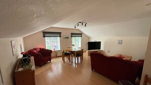 A spacious loft with a high ceiling, a dining area, two red sofas, a television, and a radiator.