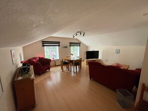 Ein geräumiger Loft mit hoher Decke, einem Essbereich, zwei roten Sofas, einem Fernseher und einer Heizung.