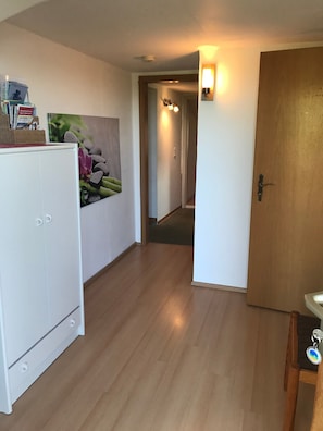 Ein Korridor mit einem weißen Schrank, einem Wandbild, einer Holztür und einer Leuchte.