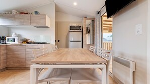 A modern kitchen with a dining table, chairs, a microwave, a refrigerator, and a TV mounted on the wall. - Mobile Home – 6 Guests with Shared Pool, Terrace, and Garden (Erdeven)