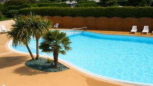 Una piscina con palmeras, sillas de descanso y una valla de madera.