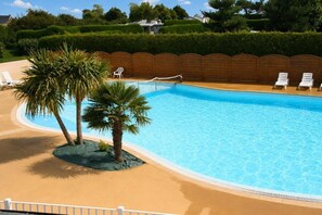 Une piscine bordée de palmiers, avec des chaises longues et une clôture en bois.