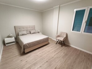 Quarto com cama, mesa de cabeceira, luminária, cadeira e janela.