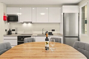 A modern kitchen with white cabinets, stainless steel appliances, and a wooden dining table with a wine bottle and glasses. - Apartment 'Ninho Ilhéu' with Mountain View and Wi-Fi (Câmara de Lobos)