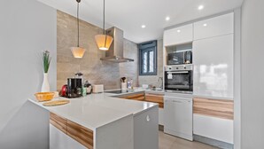 Une cuisine moderne dotée d’un îlot central, d’appareils électroménagers intégrés et de luminaires suspendus.
