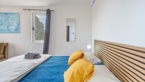 Ett sovrum med en säng, ett sängbord med en lampa, ett fönster med gardiner och en spegel som hänger på väggen.