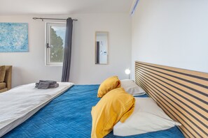 Een slaapkamer met een bed, nachtkastje met lamp, raam met gordijnen en een spiegel aan de muur.