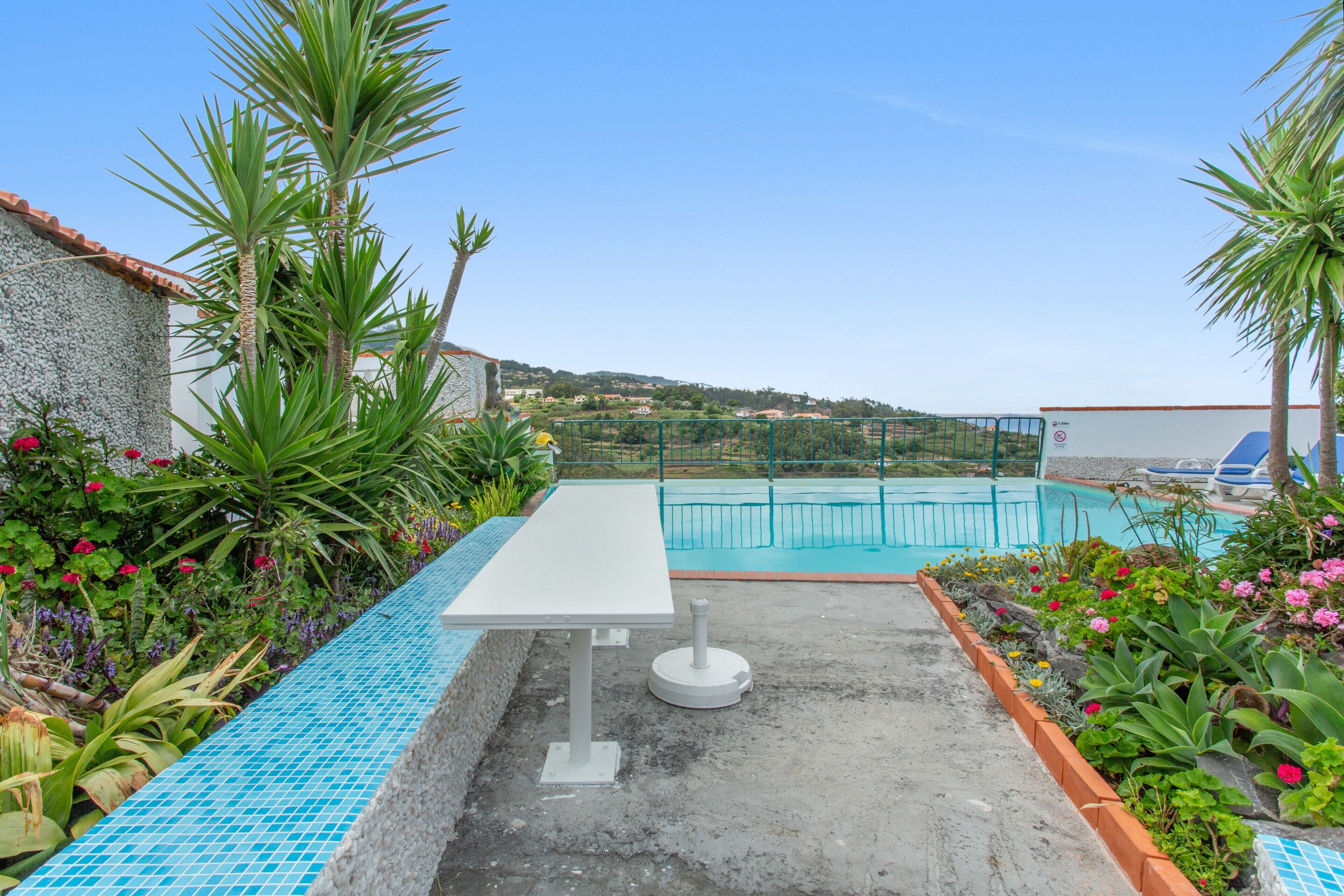 A pool area with a white table and chairs, surrounded by plants and a clear view of the pool.