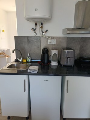 Una cocina compacta con lavamanos, cafetera, tostadora e calentador de agua.