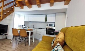Eine moderne Küche mit weißen Schränken, ein Essbereich mit Tisch und Stühlen sowie ein Wohnzimmer mit einer Couch.