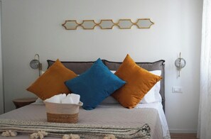 A bed with three pillows, a bedside table, a wall-mounted light, and a decorative wall piece. - Apartment 'Trabucco - Aqua Alta' with Wi-Fi and Air Conditioning (Chioggia)