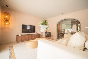 A modern living room with a flat-screen TV, a sofa, a wooden cabinet, and a glass door leading to another room. - CostaBlancaDreams - Villa Mariposa in Jávea (Javea)